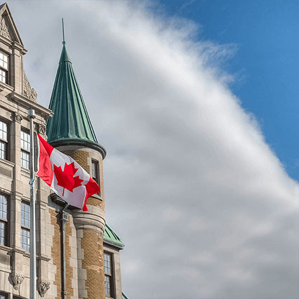 A Canadian flag flying beside a historic federal government building, representing secure, modern digital services and trusted networks supporting federal operations across Canada.