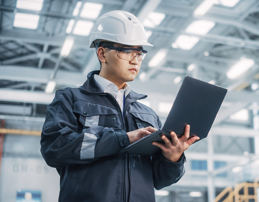Employee in a manufacturing facility using a laptop leveraging Industry 4.0 technologies and IoT.