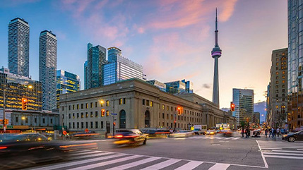 A busy urban intersection at dusk with moving traffic and a city skyline in the background, illustrating how IoT supports real-time monitoring, analytics and smarter municipal operations to improve efficiency and the overall citizen experience.