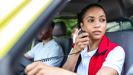 A public safety responder inside an emergency vehicle using a handheld radio, symbolizing Bell’s public safety solutions with P25 radio, CAD technologies, and critical network applications that deliver reliable communication when every second matters.