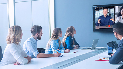 Colleagues in an office attending a meeting around a conference table and connecting with remote workers on a video call using a voice and collaboration solution from Bell.